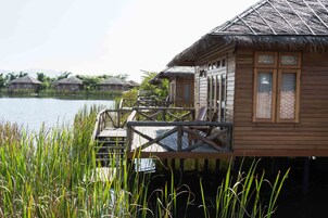 A wooden house with a thatched roof, a wooden deck, and a view of a lake.