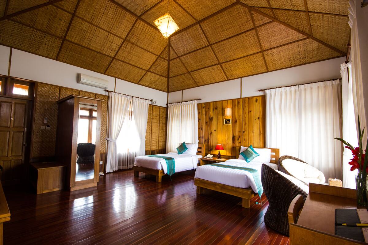Ein Zimmer mit zwei Betten, Holzboden, einem Reetdach und einem Holztisch mit Stuhl.