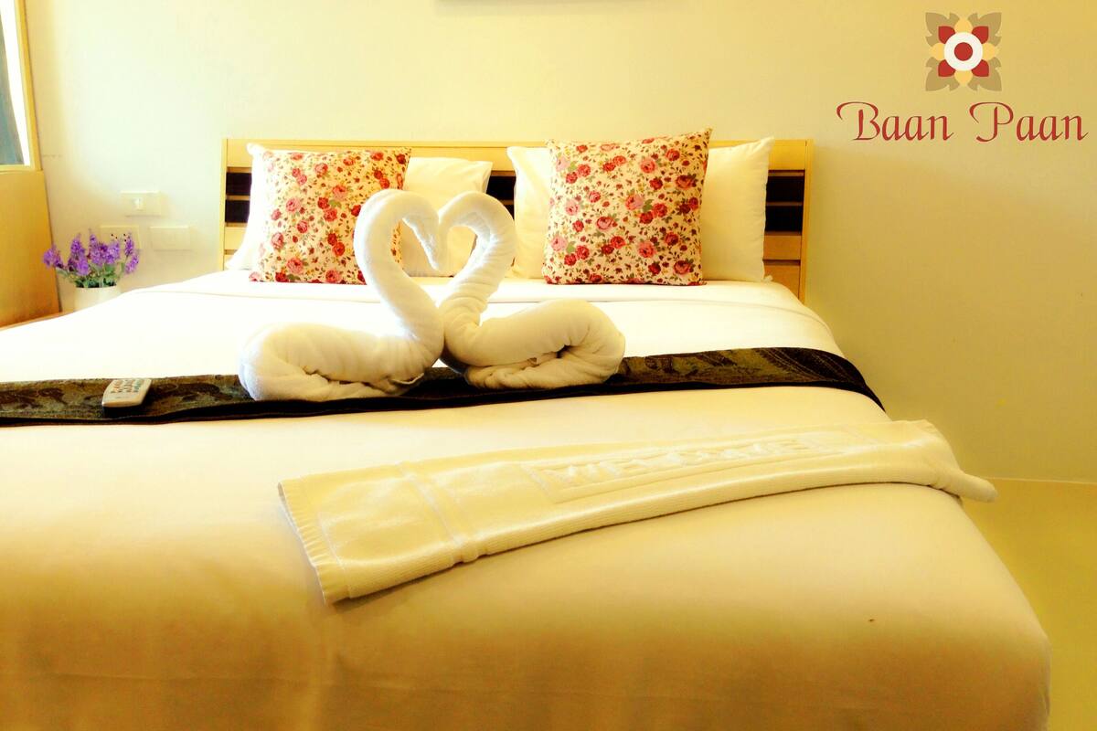 A neatly made bed with a heart-shaped towel arrangement, floral pillows, and a bedspread.