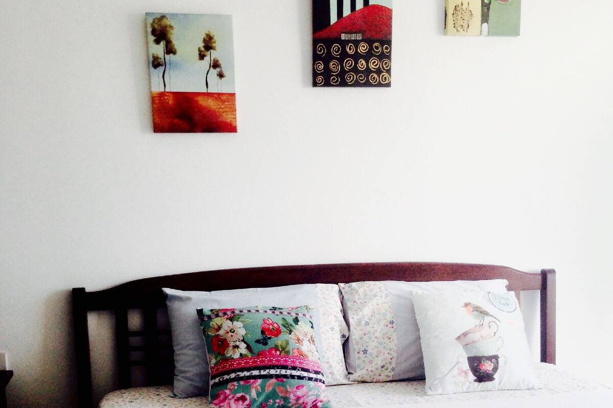 A neatly made bed with a white duvet and folded towels, a wooden headboard, and floral-patterned pillows.