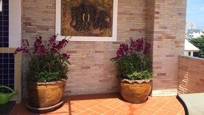 A tiled patio with two large potted plants, a framed painting of elephants, and a view of a building in the background. - Baan Paan Hua Hin (Hua Hin)