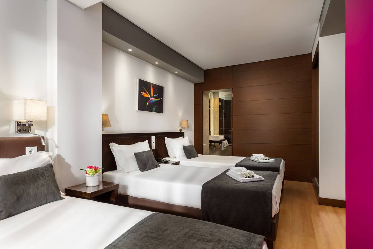 Ein Hotelzimmer mit zwei Betten, einem Nachttisch mit Lampe, einem kleinen Tisch mit Blumenvase und einem Bild an der Wand.
