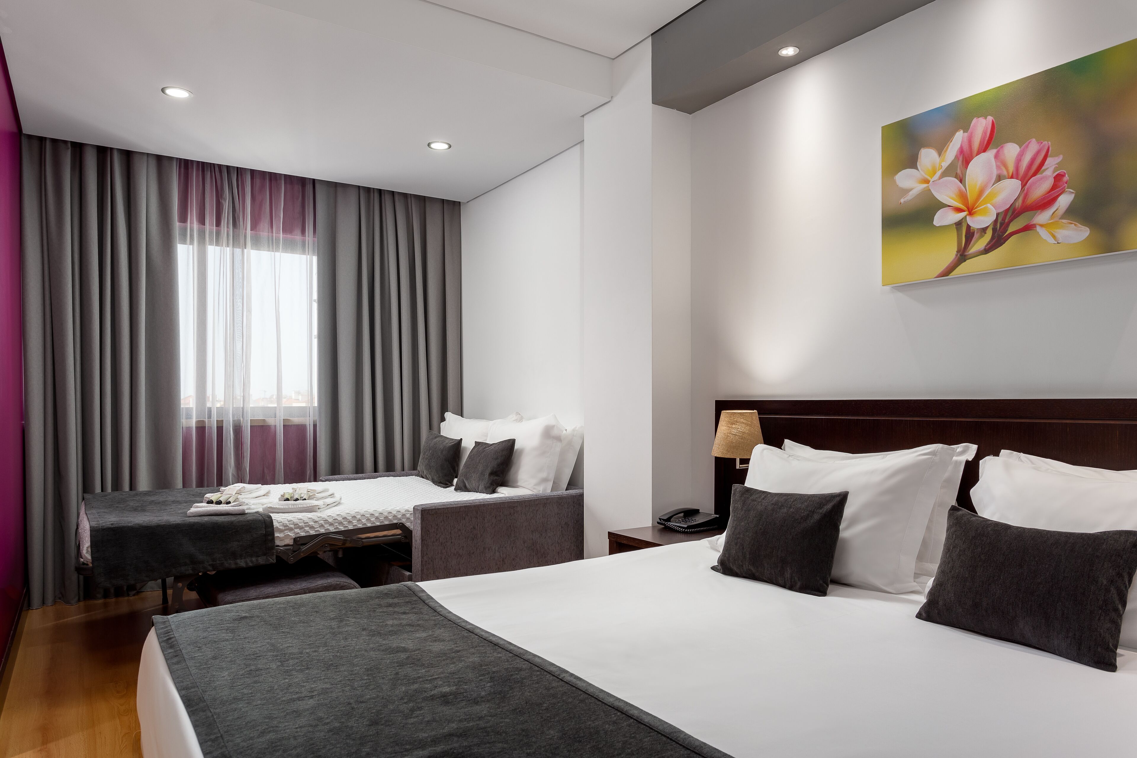 Une chambre d’hôtel avec un grand lit, deux petits lits, un bureau et une fenêtre avec des rideaux.