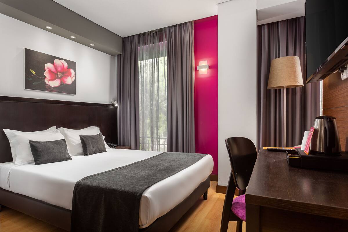 Ein Hotelzimmer mit einem großen Bett, einem Schreibtisch mit Lampe und einem Fernseher.