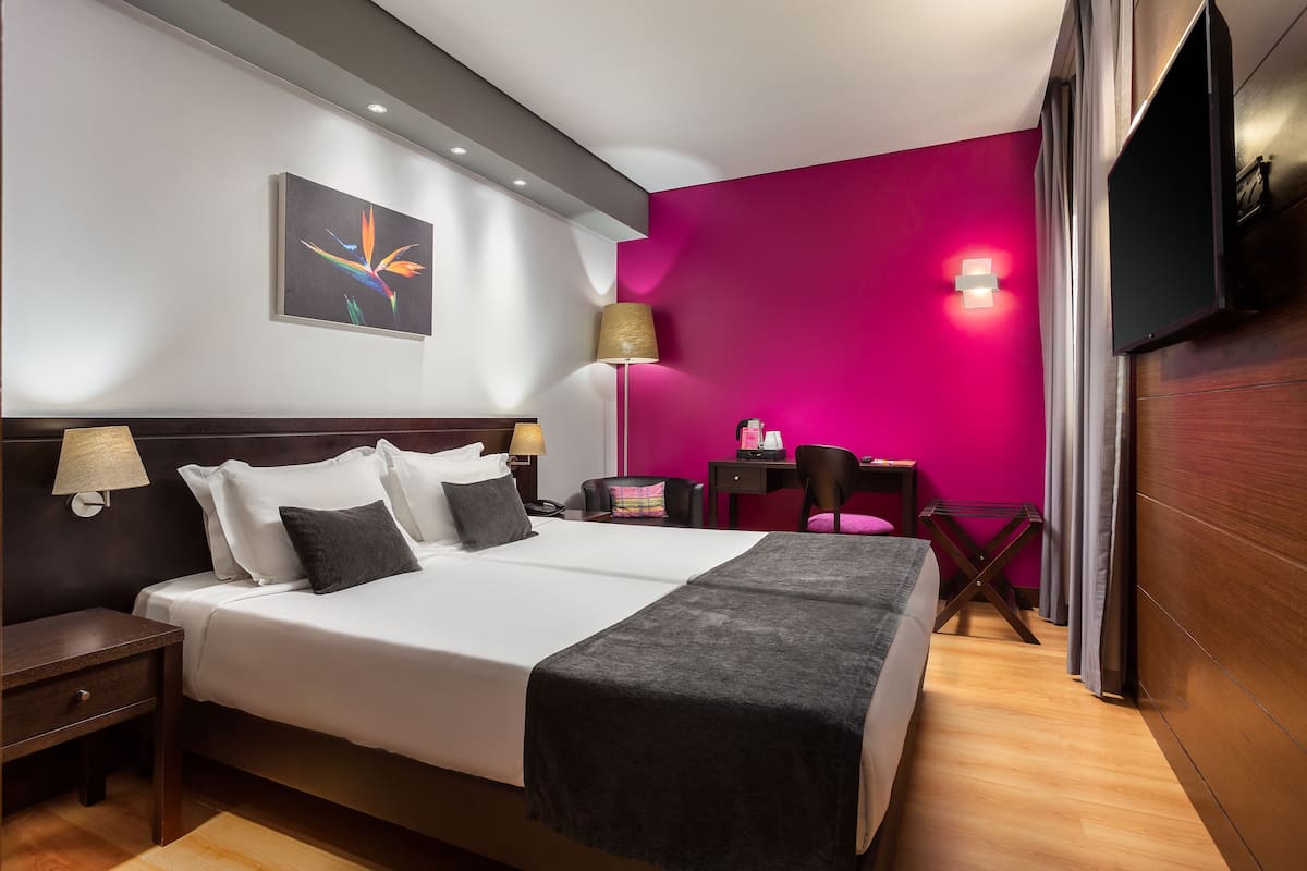 Ein Hotelzimmer mit Bett, Nachttischen, Schreibtisch, Stuhl, Lampe, Fernseher und einem Bild an der Wand.