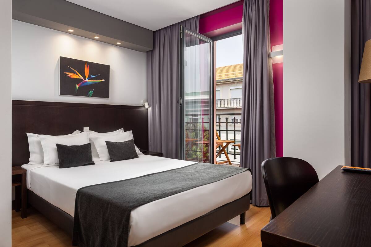 Ein modernes Hotelzimmer mit einem großen Bett, einem Schreibtisch und einem Balkon mit Vorhängen.