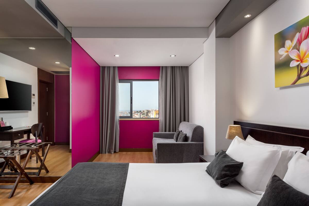 Ein Hotelzimmer mit Bett, Schreibtisch, Stuhl, Fernseher und einem fenster mit Vorhängen.
