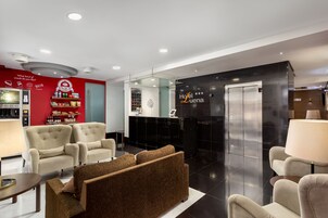 Un'accogliente hall di un hotel moderno con una parete rossa, una reception, un angolo bar e una zona relax con divani.