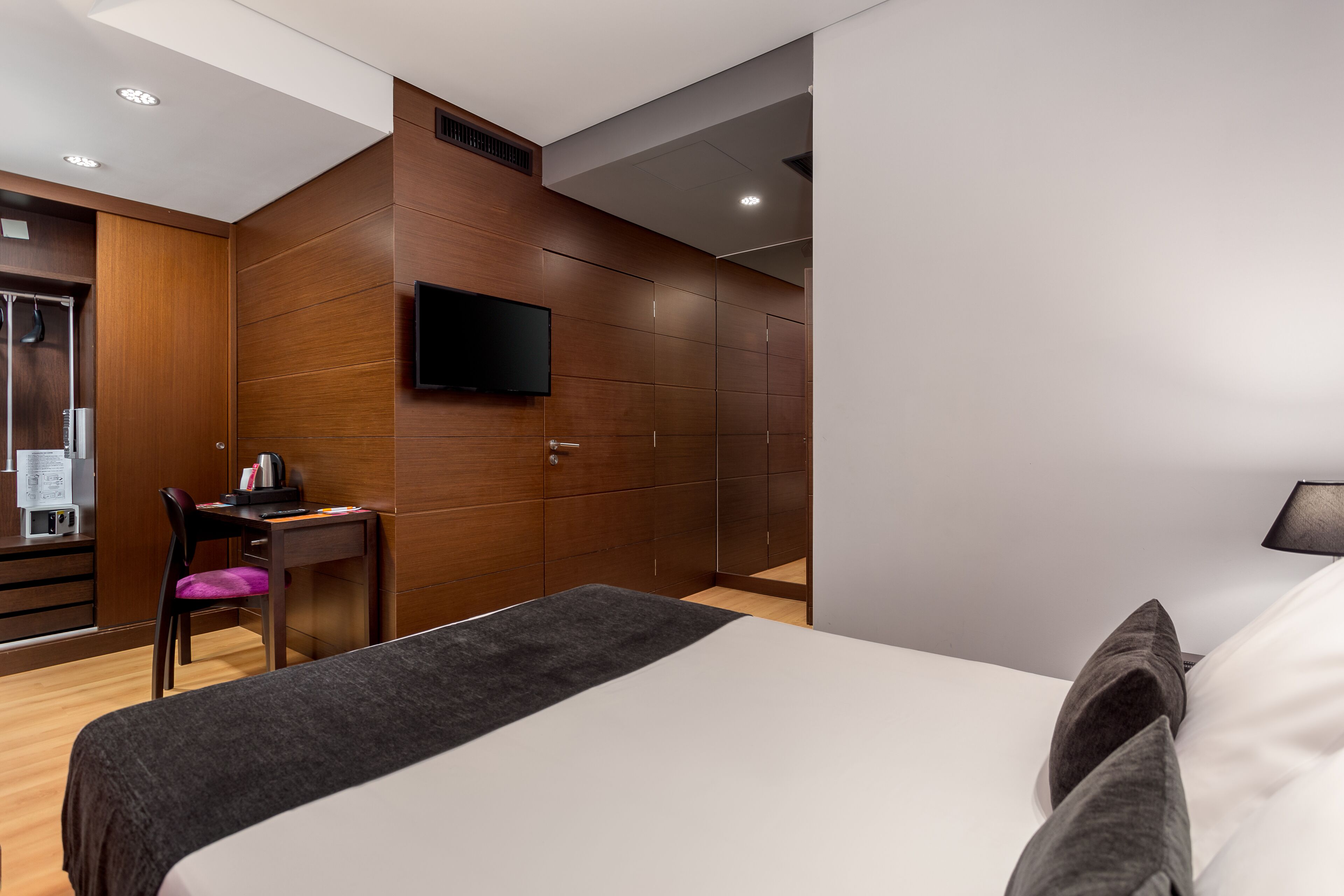 Une chambre d’hôtel moderne équipée d’un lit, d’un bureau avec une chaise, d’un téléviseur à écran plat fixé au mur et d’une armoire.