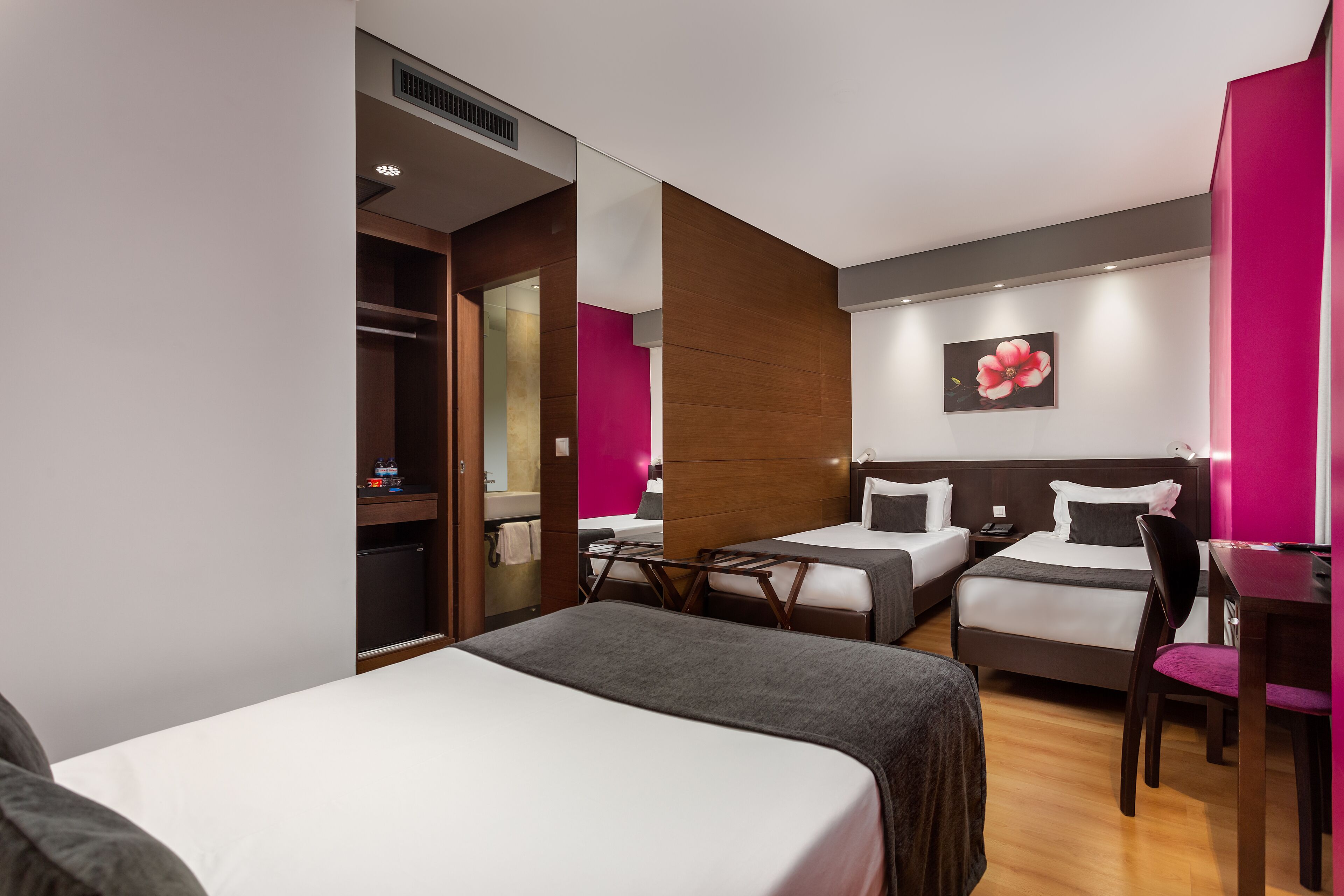 Une chambre d’hôtel avec deux lits, un bureau, une chaise, un miroir et une salle de bain visible à travers une porte ouverte.