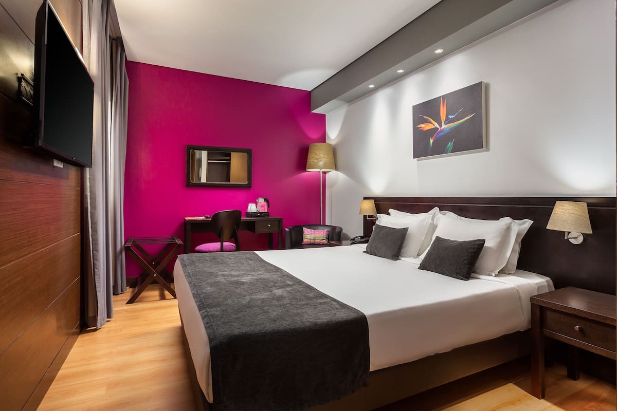 Ein Hotelzimmer mit einem großen Bett, einem Schreibtisch, einem Stuhl und einem Fernseher.