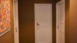 Un pasillo con suelo alfombrado, una puerta blanca y un cuadro abstracto de colores en la pared.