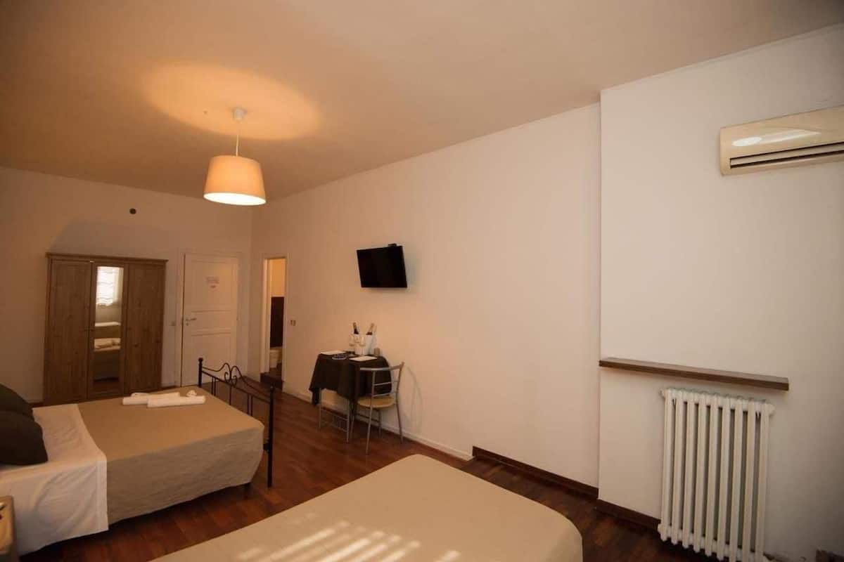 A bedroom with two beds, a table with a chair, a TV mounted on the wall, and an air conditioning unit.