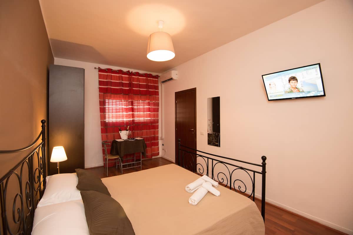 A hotel room with a bed, a desk, a chair, a television, and a window with red curtains.