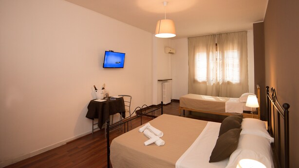 Habitación de hotel con cama, escritorio, silla, televisor y ventana con cortinas.