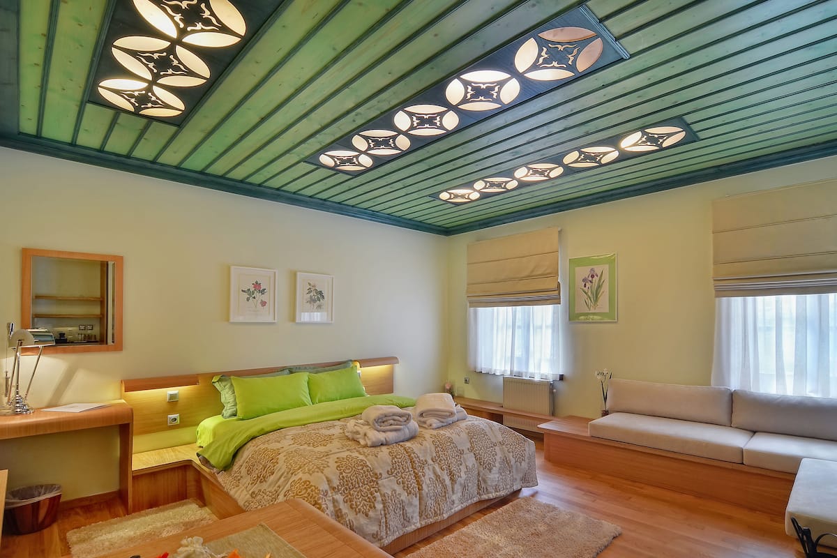 A bedroom with a bed, bedside tables, a desk, a sofa, and a ceiling with decorative lights.