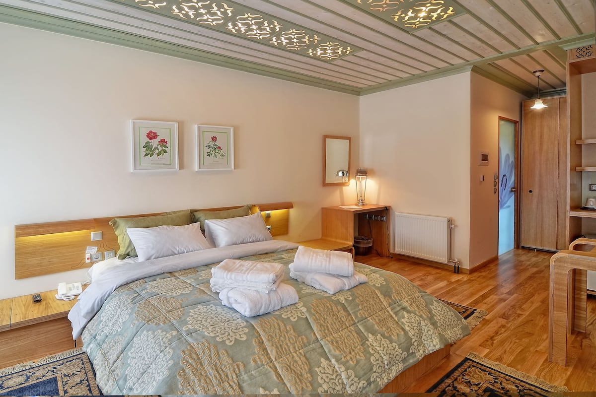 A neatly made bed with a patterned bedspread and pillows, a bedside table with a lamp, and two framed floral artworks on the wall.