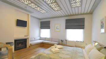 A modern bedroom with a fireplace, a sofa bed, and a large bed with a patterned bedspread.
