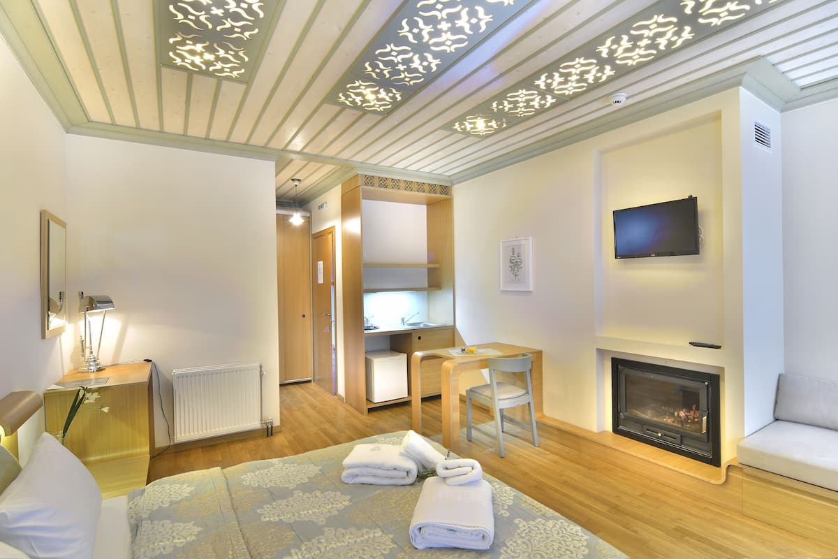 A hotel room with a bed, a desk, a chair, a fireplace, and a television.