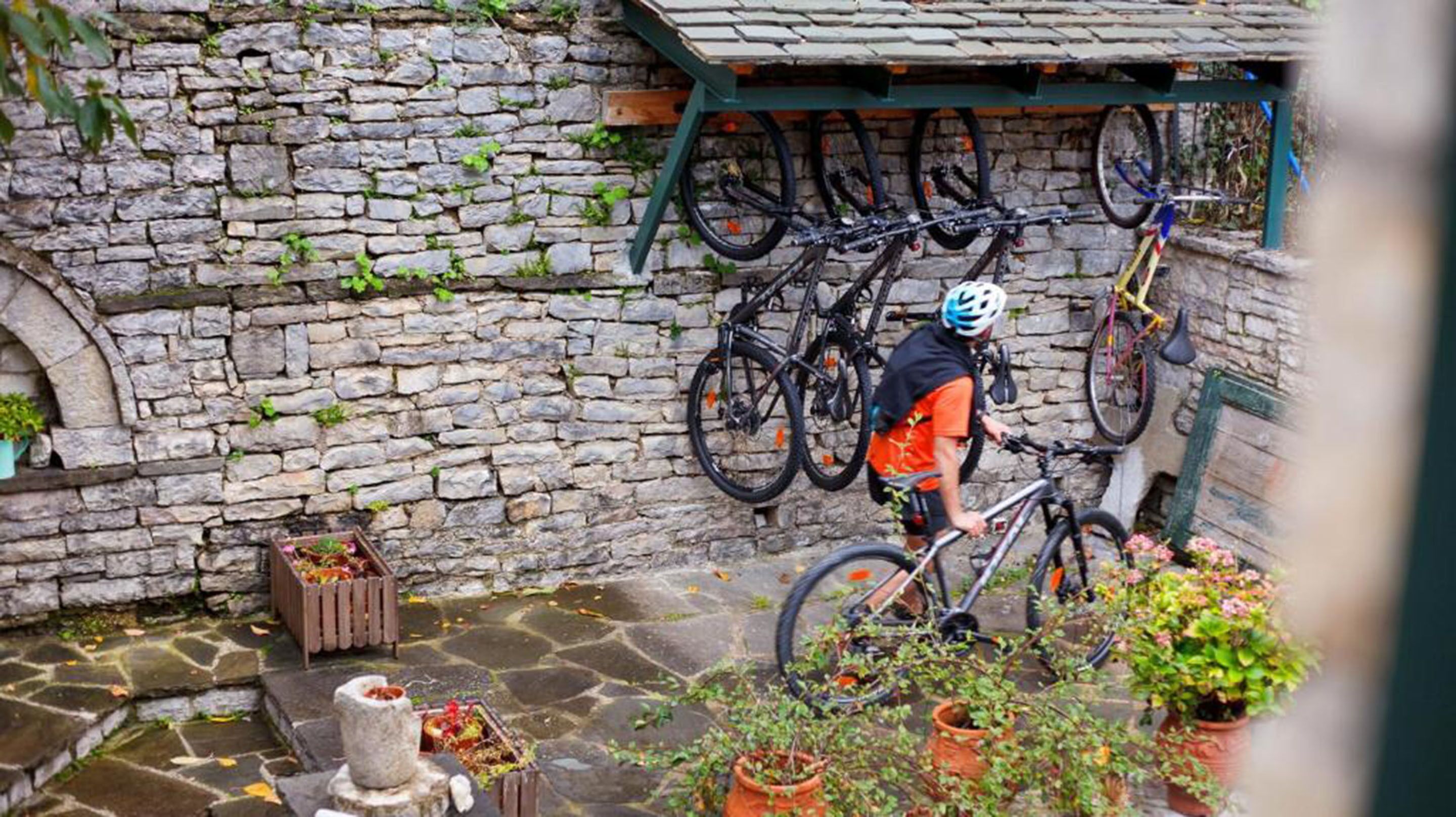 A stone wall with bicycles mounted on it, a person riding a bike, and potted plants around.
