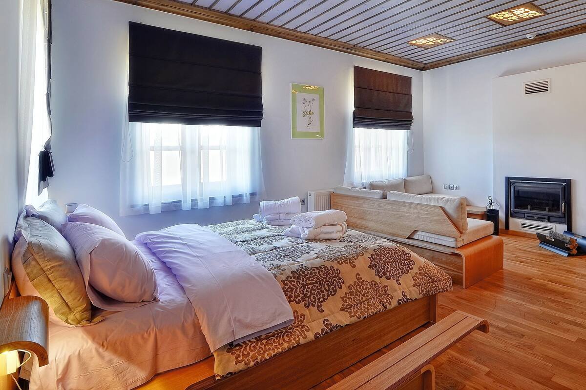 A bedroom with a large bed, a smaller bed, a wooden bench, a fireplace, and a TV.