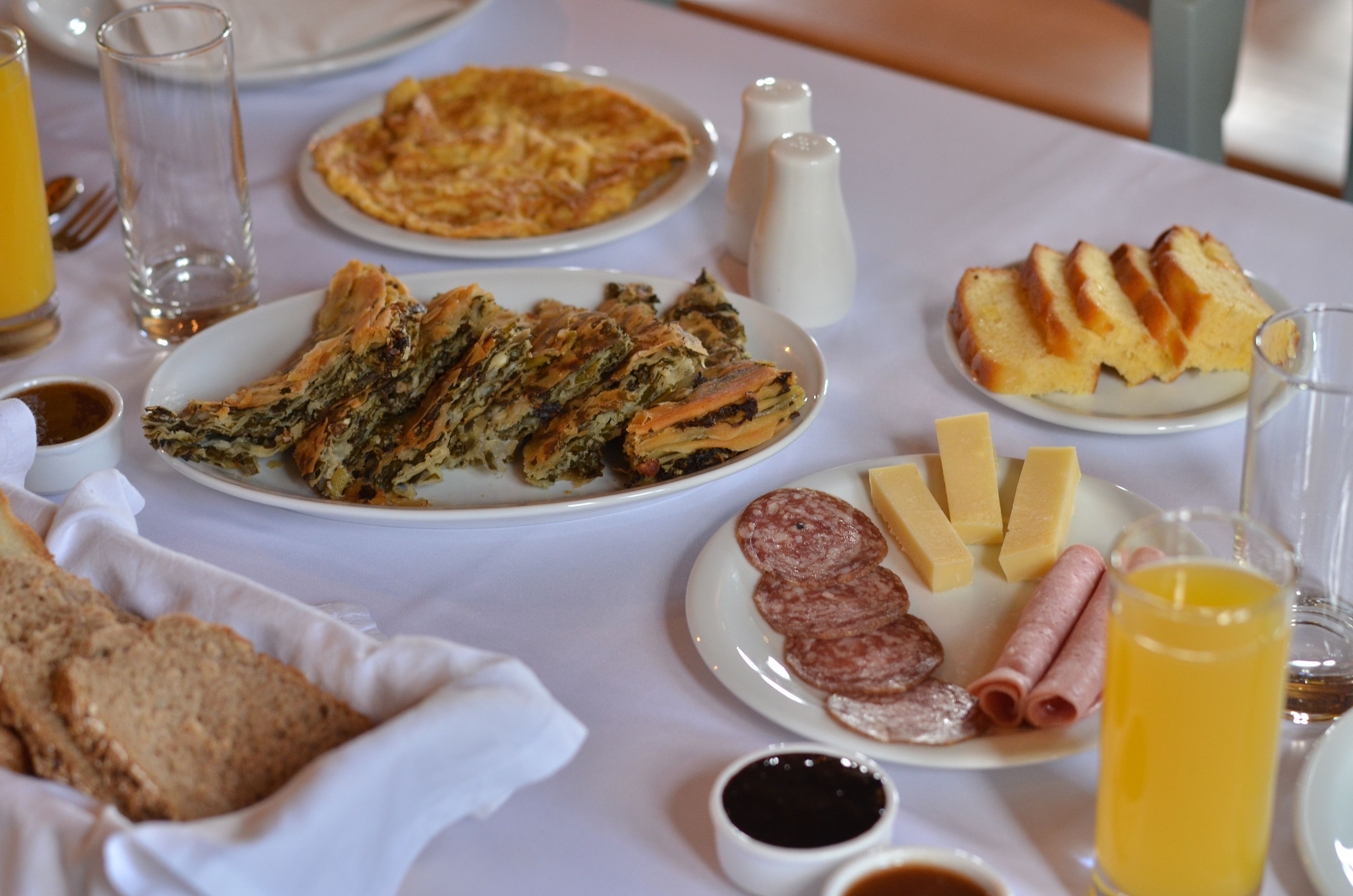 Una mesa de desayuno con varios platos, incluyendo una frittata, una rebanada de pan, queso y embutidos.