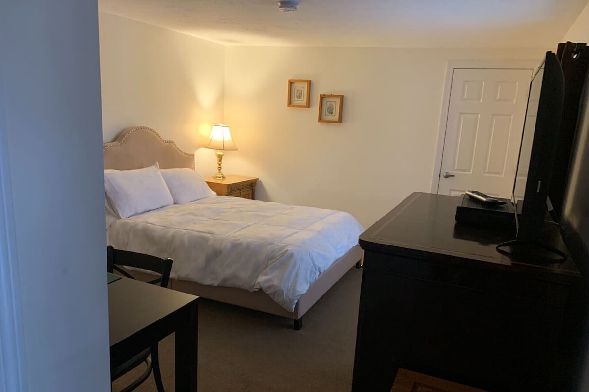 Une chambre d’hôtel comprenant un lit, une table de chevet avec une lampe, un bureau, une chaise et un téléviseur.