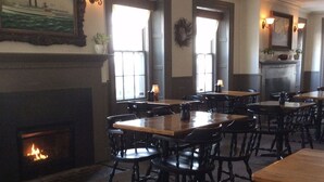 Un espace repas comprenant plusieurs tables et chaises, une cheminée et un tableau accroché au mur.