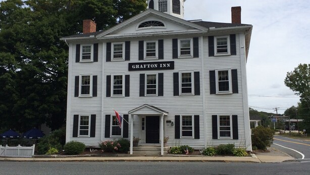 Un bâtiment blanc avec des volets noirs, une enseigne indiquant « Grafton Inn » et un petit drapeau.