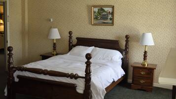 A neatly made bed with a wooden frame and white linens, two bedside tables with lamps, a framed picture on the wall, and a carpeted floor.