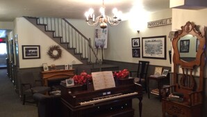 Un salon agrémenté d’un magnifique piano à queue, d’un lustre, d’un escalier et de tableaux encadrés accrochés aux murs.