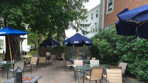 Un espace extérieur aménagé en terrasse, avec des tables et des chaises, protégé par des parasols, et doté d’un barbecue.