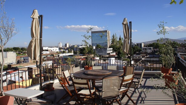 A rooftop terrace with a round table and chairs, surrounded by potted plants and umbrellas. - Suites Chapultepec (Guadalajara)