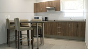 A modern kitchen with wooden cabinets, a microwave, and a coffee maker. There are two bar stools and a small table. - Suites Chapultepec (Guadalajara)