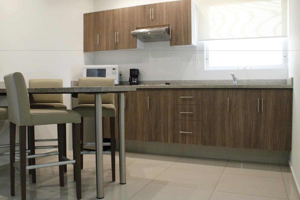 Una cocina moderna con armarios de madera, un microondas y una cafetera. Hay dos taburetes de bar y una mesita.