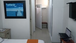 A hotel room with a bed, a desk with a laptop, a painting of a pier, and a view of a corridor. - Suites Chapultepec (Guadalajara)