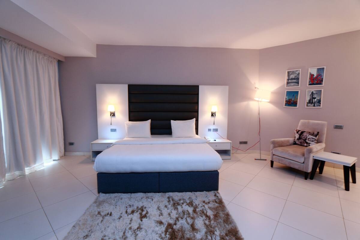 A modern bedroom with a large bed, bedside tables, a chair, and artwork on the wall.