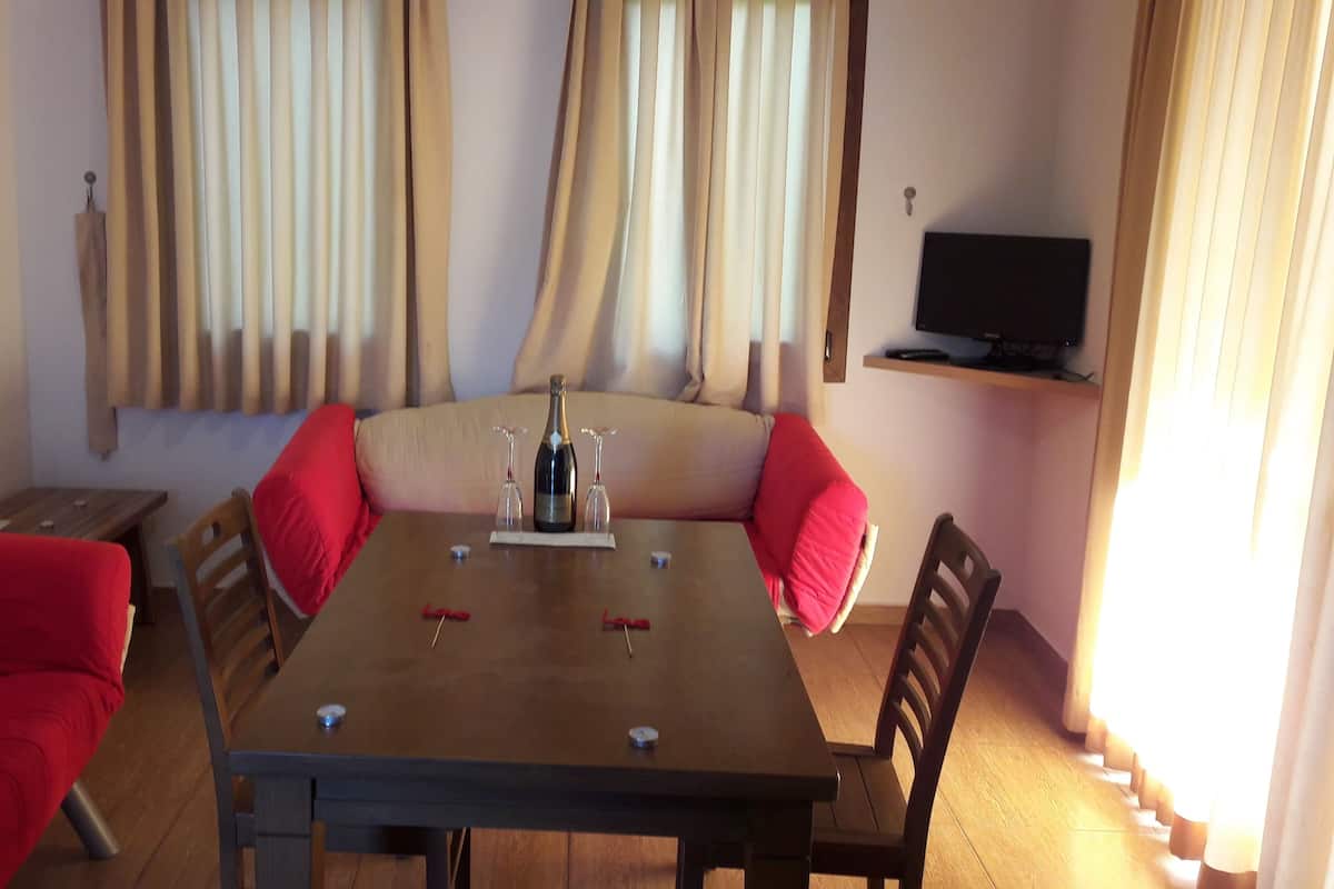 Un comedor con una mesa de madera, cojines rojos y una botella de champán sobre un soporte.