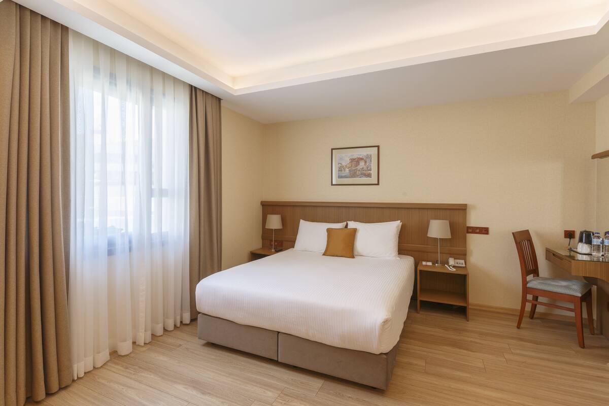 A hotel room with a large bed, a desk, a chair, and a nightstand.