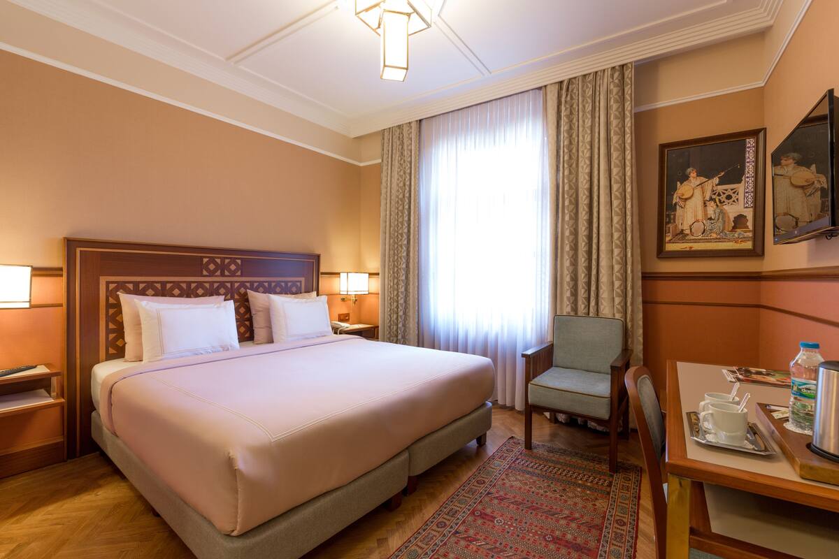 A hotel room with a large bed, a sitting area with a chair, a table with a tray, and a painting on the wall.
