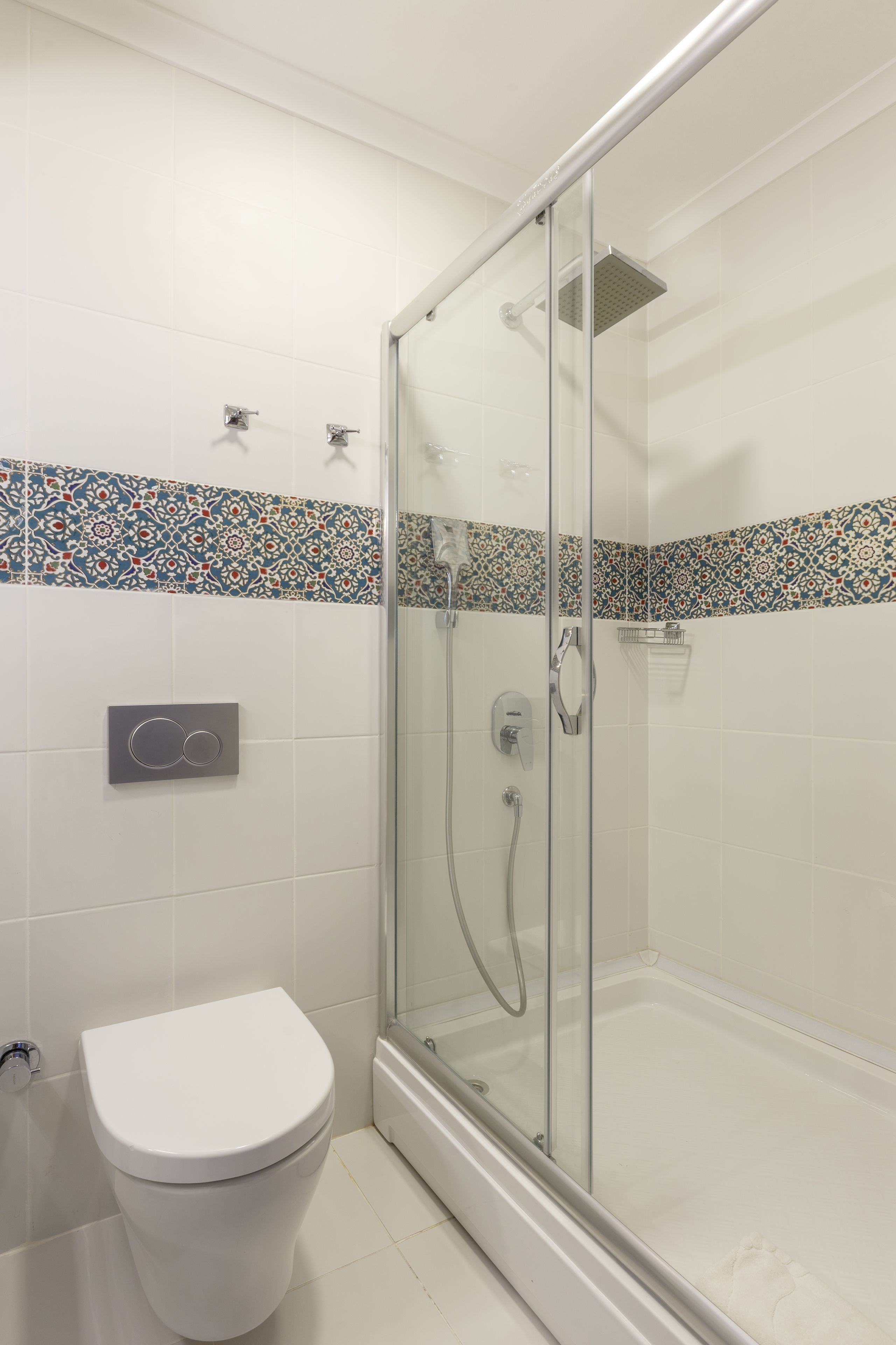 Un baño con cabina de ducha de vidrio, inodoro y pared de azulejos con un detalle decorativo.