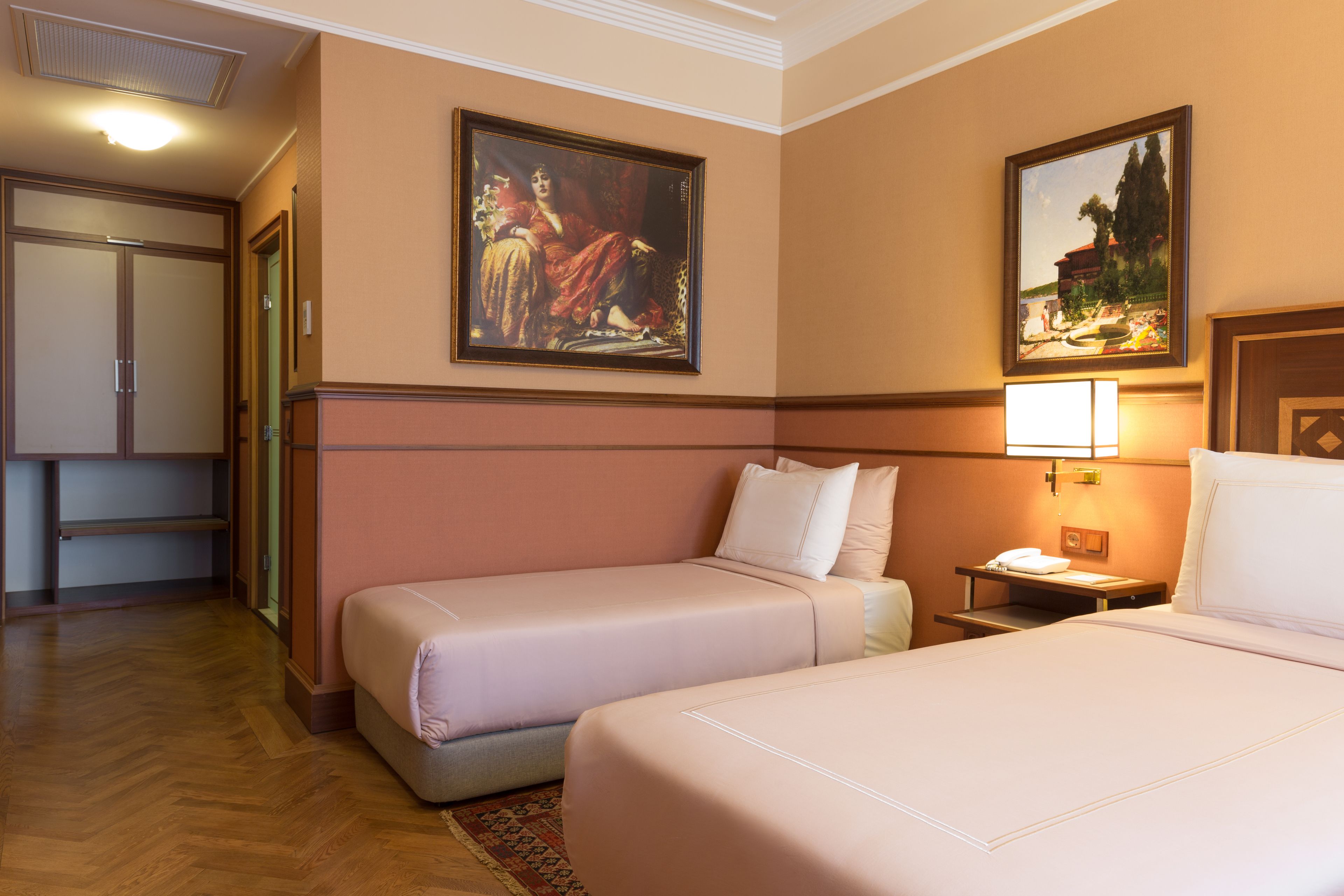 Een hotelkamer met twee bedden, een nachtkastje, een lamp en twee ingelijste schilderijen aan de muur.