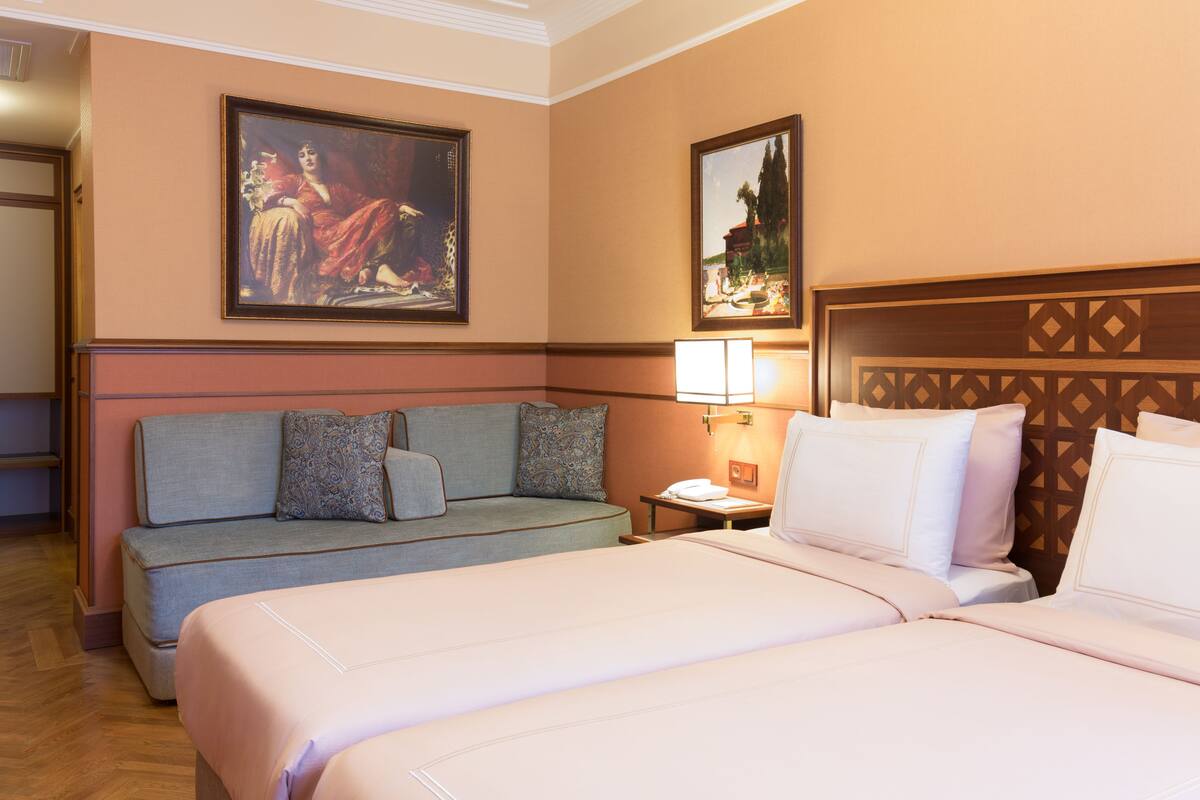 A hotel room with a bed, a sofa, a nightstand, and two paintings on the wall.