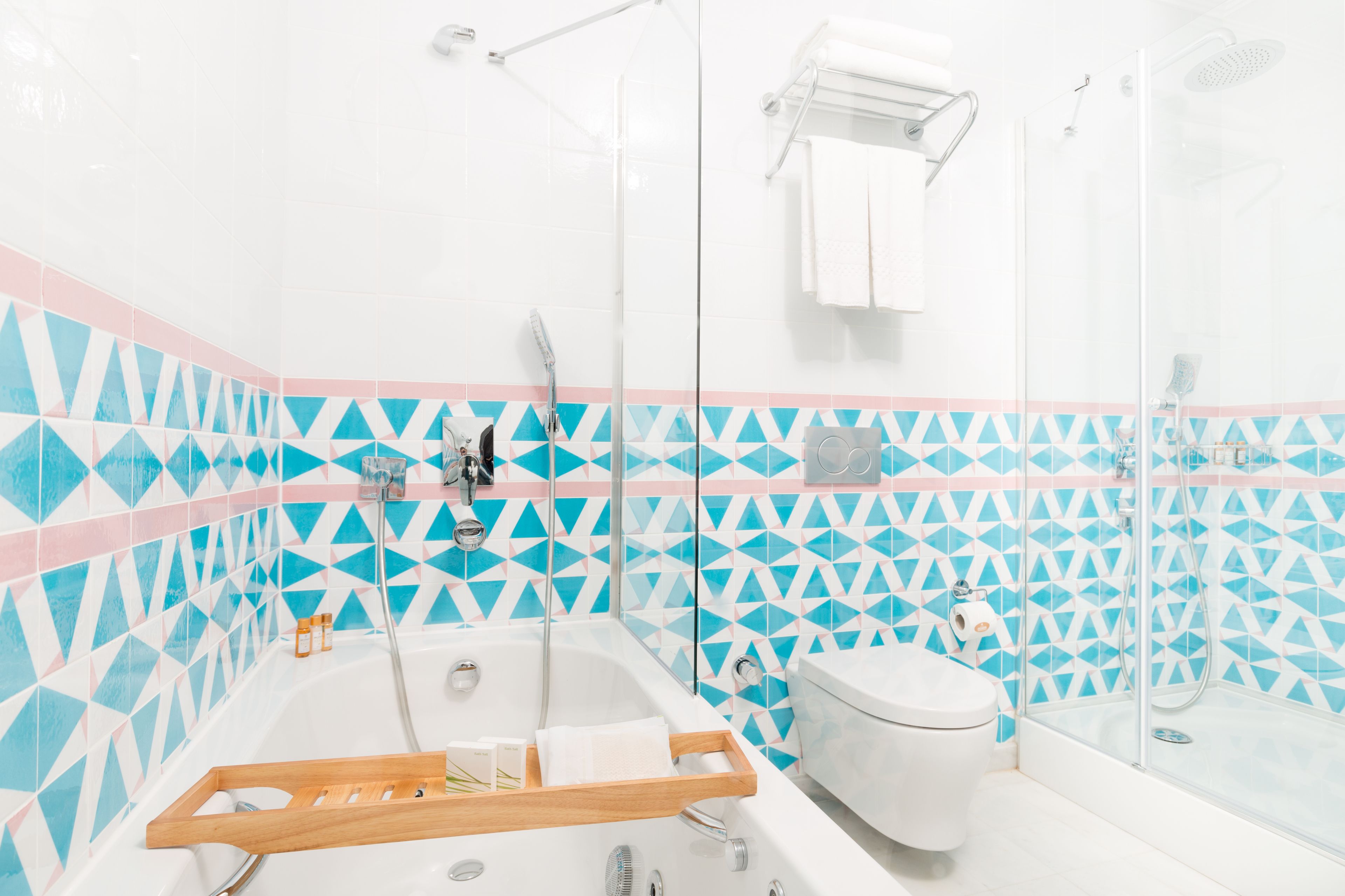 A modern bathroom with a geometric tile pattern, a bathtub, a toilet, and a glass-enclosed shower area.