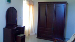 A room with a large wardrobe, a desk with a chair, and a small stool. - La Residnce les Badamiers (Trou d'Eau Douce)