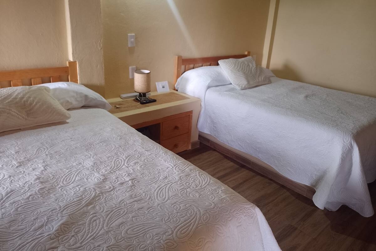 A hotel room with two single beds, a wooden desk, a lamp, and a nightstand.