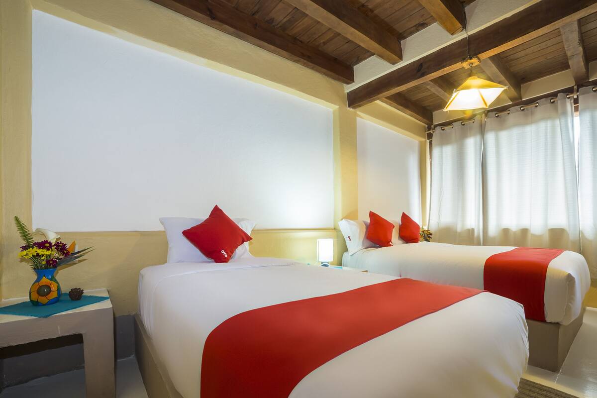 A hotel room with two beds, each with red and white bedding, a nightstand with a vase of flowers, and a wooden ceiling.