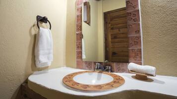 A bathroom with a white sink, a mirror with a leaf-patterned frame, and a towel hanging on a hook.