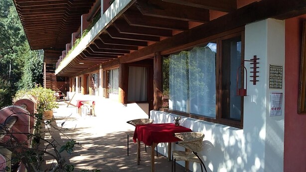 Eine Terrasse im Freien mit Holzbalken, einem Tisch mit roter Tischdecke, Korbstühlen und einem Grill.