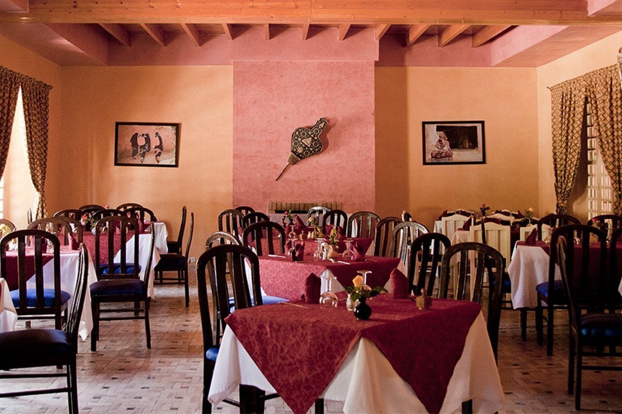 Un comedor con mesas dispuestas para el servicio, sillas de madera y un elemento decorativo en la pared.